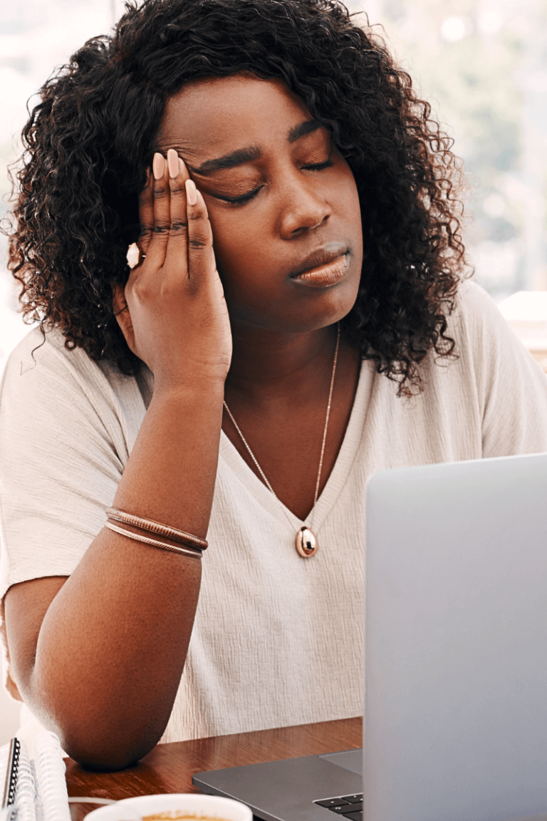 Stressed working mom with her head in her hand while using a laptop, symbolizing burnout and mom guilt.